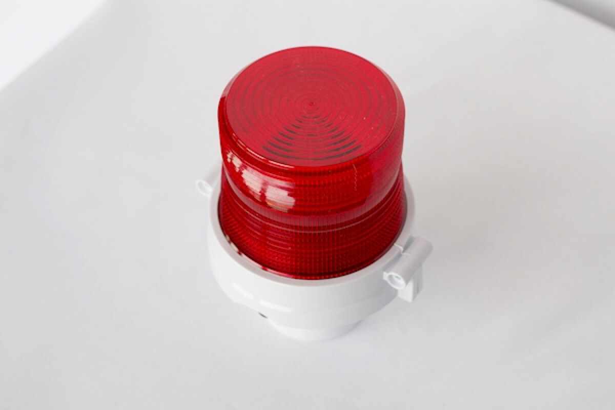 Red industrial warning beacon light with a white mounting base, typically used for emergency alerts or hazard signaling.